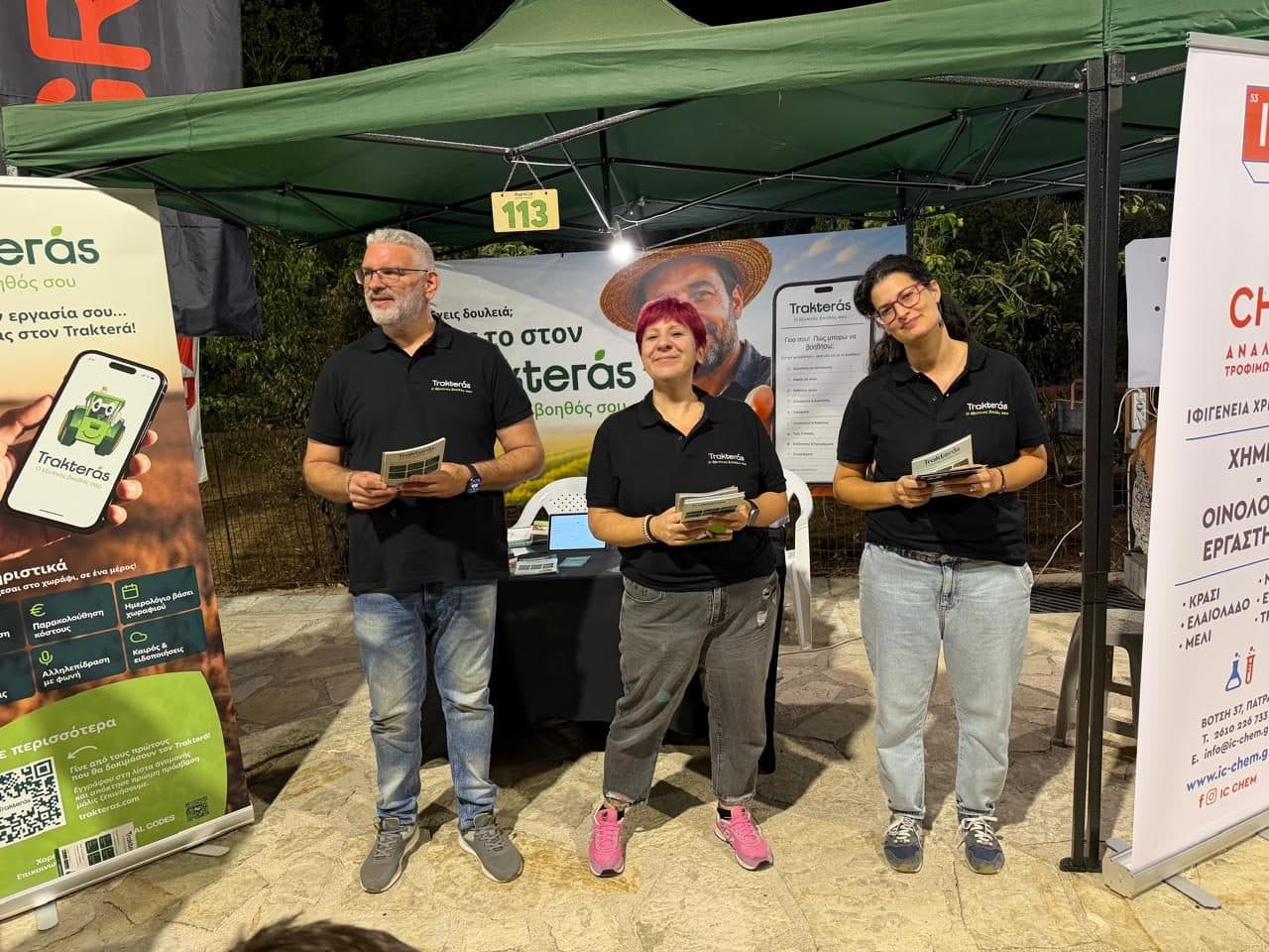 Three members of the Trakterás team at the fair stand, wearing branded shirts and holding leaflets